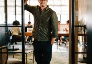 A man smiling and standing in an open doorway to an office