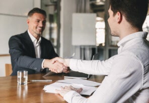 Business, career and placement concept - successful young man smiling and handshaking with european businessman after successful negotiations or interview in office