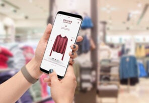 A person using their phone to shop for clothes while also walking inside a clothing store