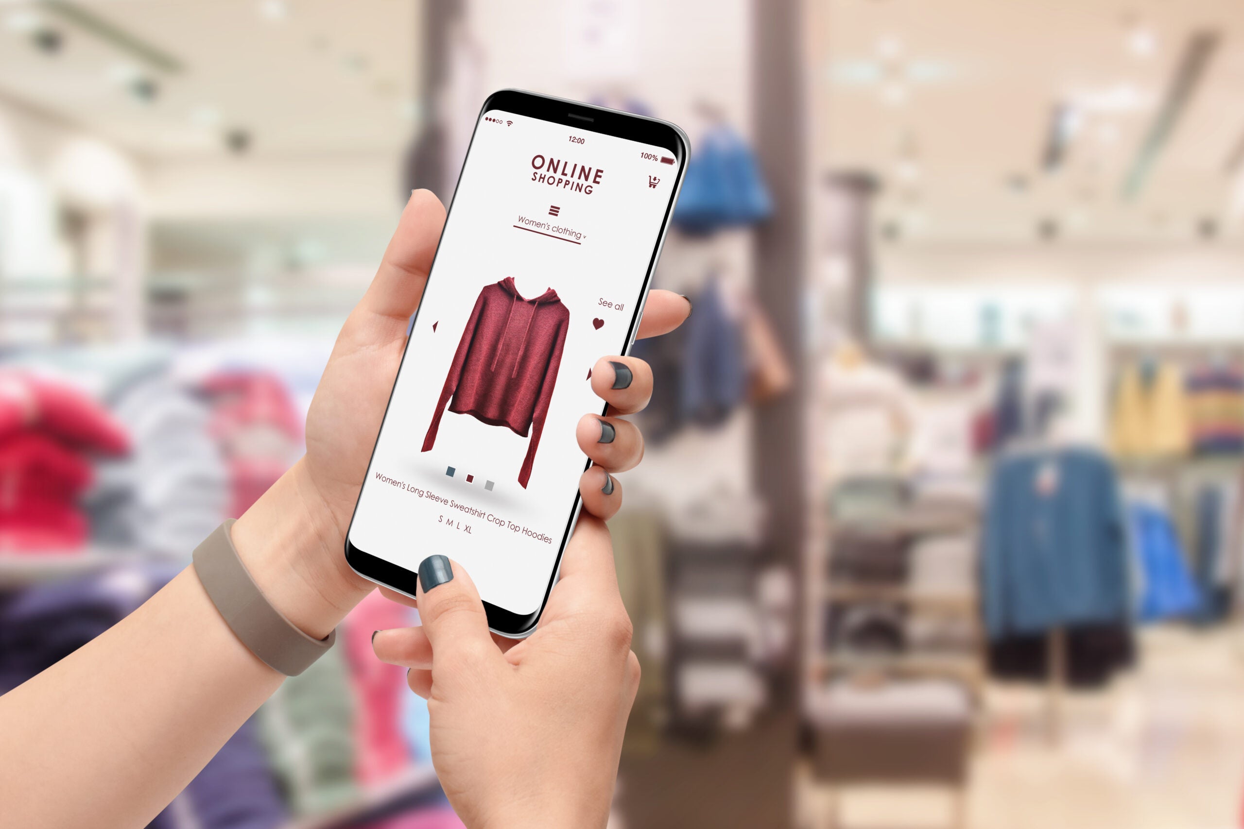 A person using their phone to shop for clothes while also walking inside a clothing store