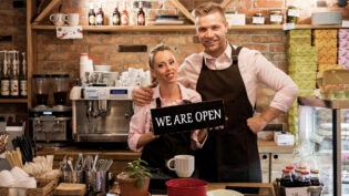 two business owners proudly displaying their "We Are Open" sign in their newly opened cafe