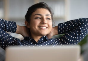 Happy satisfied indian woman rest at home office sit with laptop hold hands behind head, dreamy young lady relax finished work feel peace of mind look away dream think of future success concept