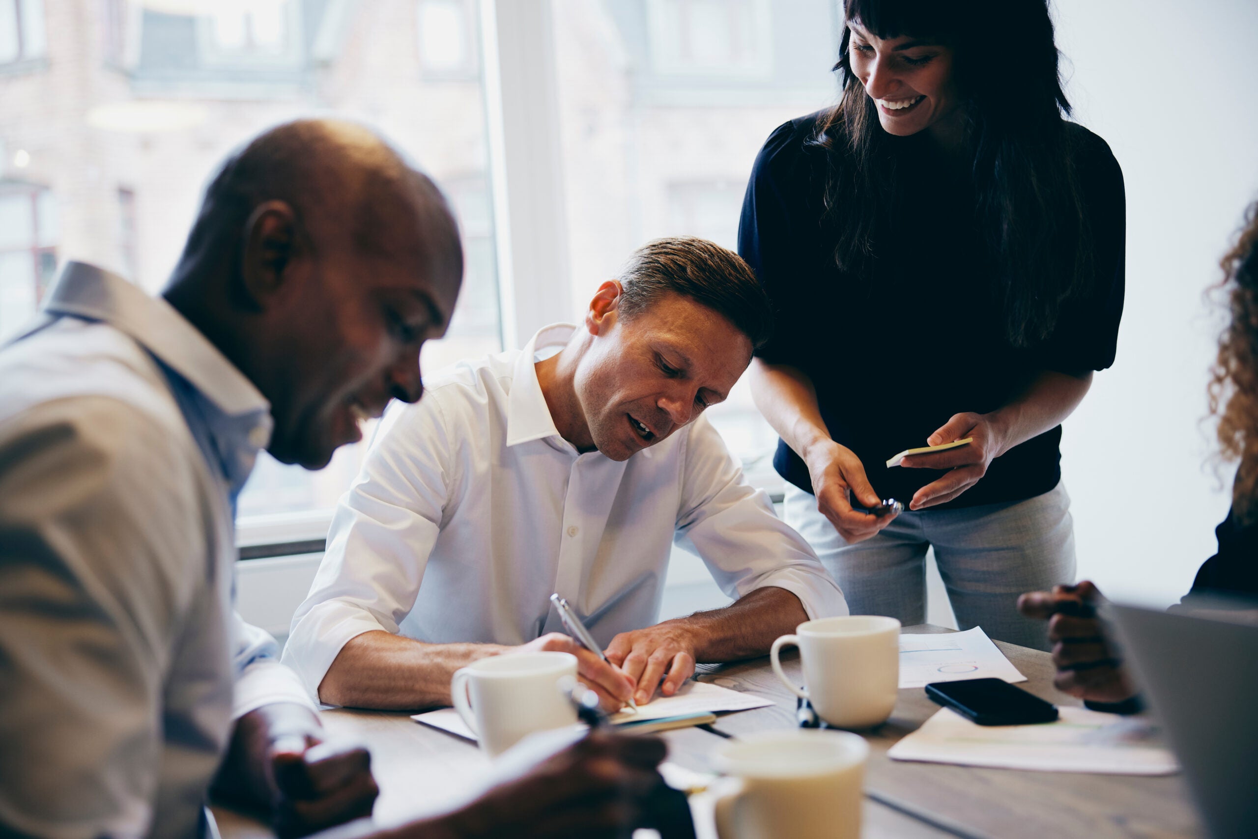 Manager signing paperwork while working with a diverse team of colleagues around a boardroom table in an office