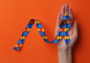 a hand holding a neurodiverse themed ribbon