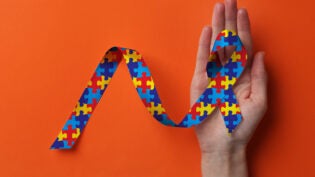 a hand holding a neurodiverse themed ribbon