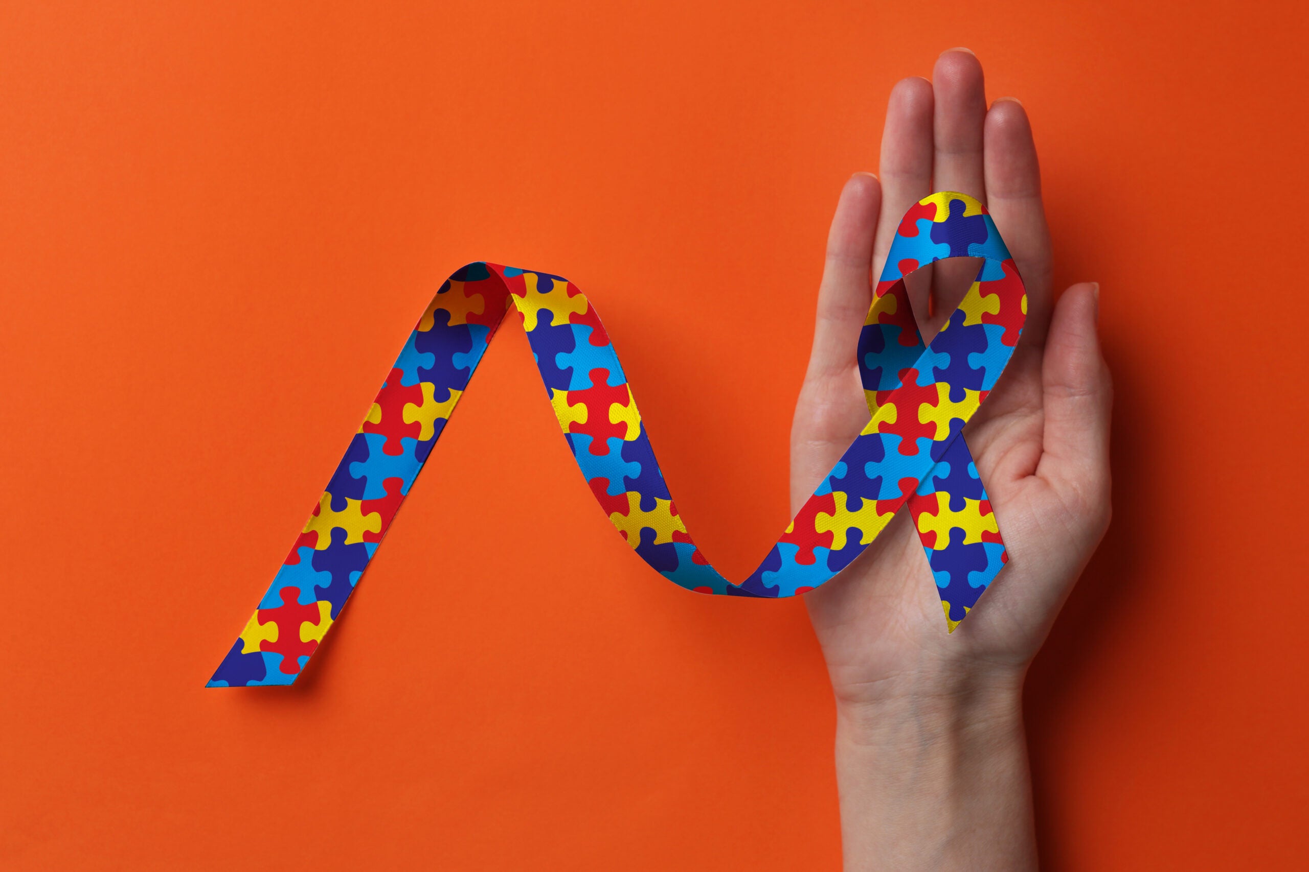 a hand holding a neurodiverse themed ribbon