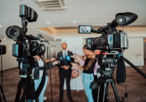 video cameras pointed at a man giving an interview to a group of reporters