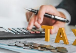 a close up view of a hand using a calculator with the word "TAX" in bold block-like letters