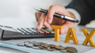 a close up view of a hand using a calculator with the word "TAX" in bold block-like letters