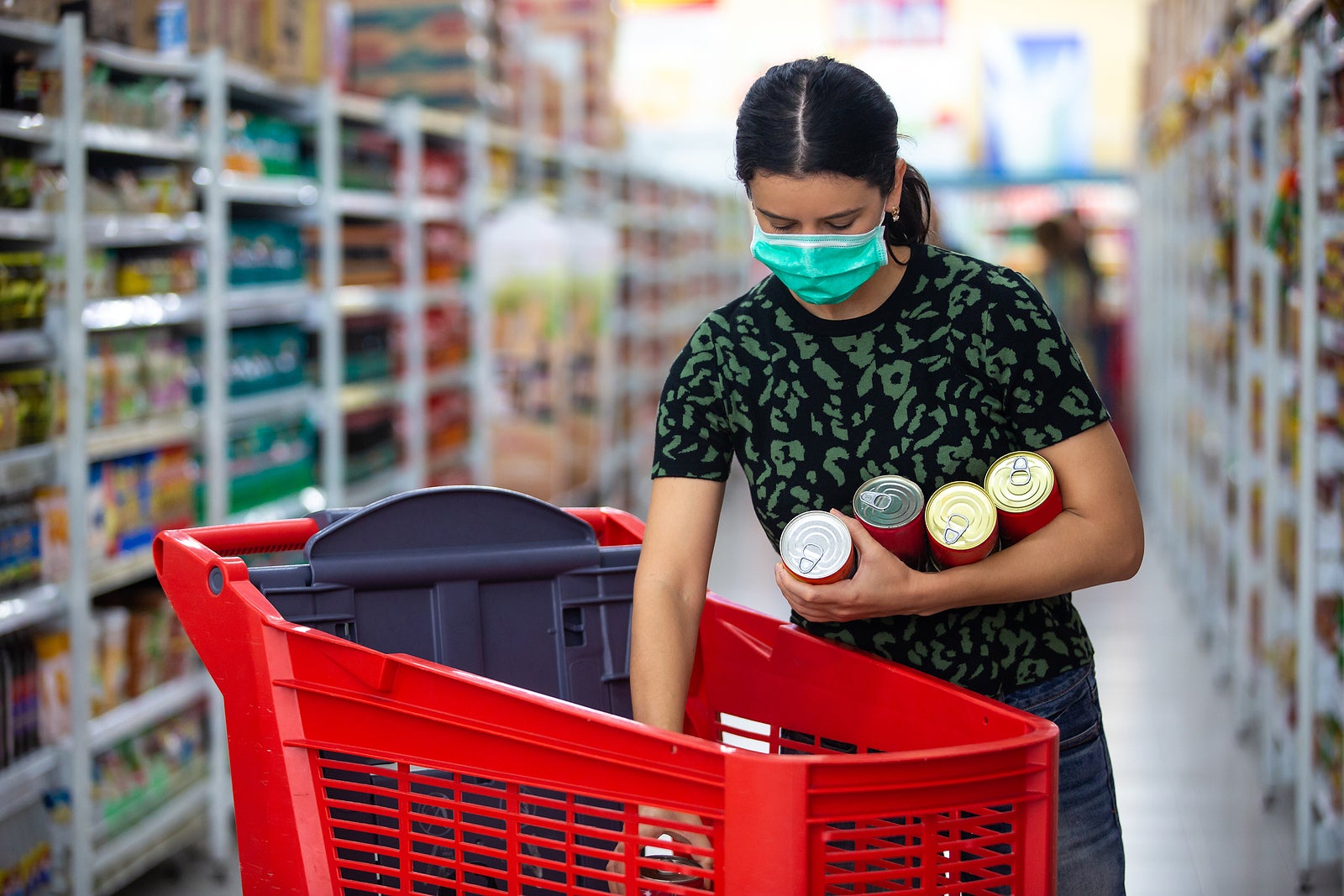 Alarmed female wears medical mask against coronavirus while grocery shopping in supermarket or store- health, safety and pandemic concept - young woman stockpiling food in fear of covid-19