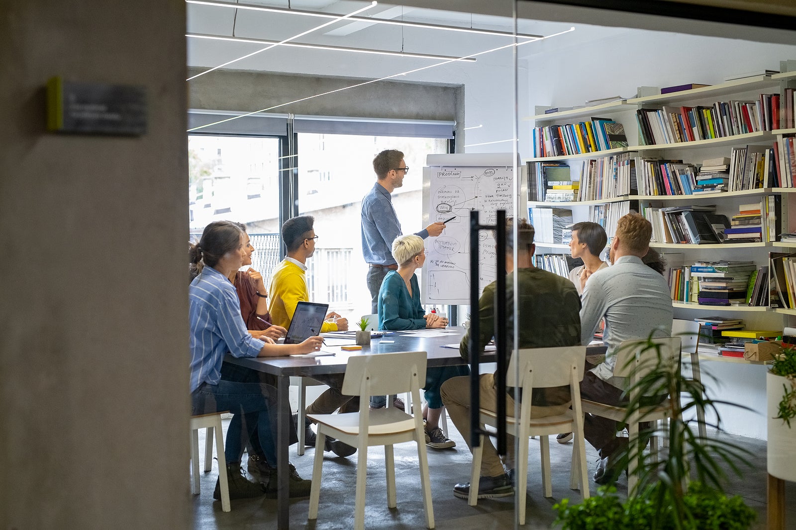 Businessman giving a presentation to multiethnic creative team at office. Business brief with annual goals with employees. Leadership man training businessmen and businesswomen in conference room.