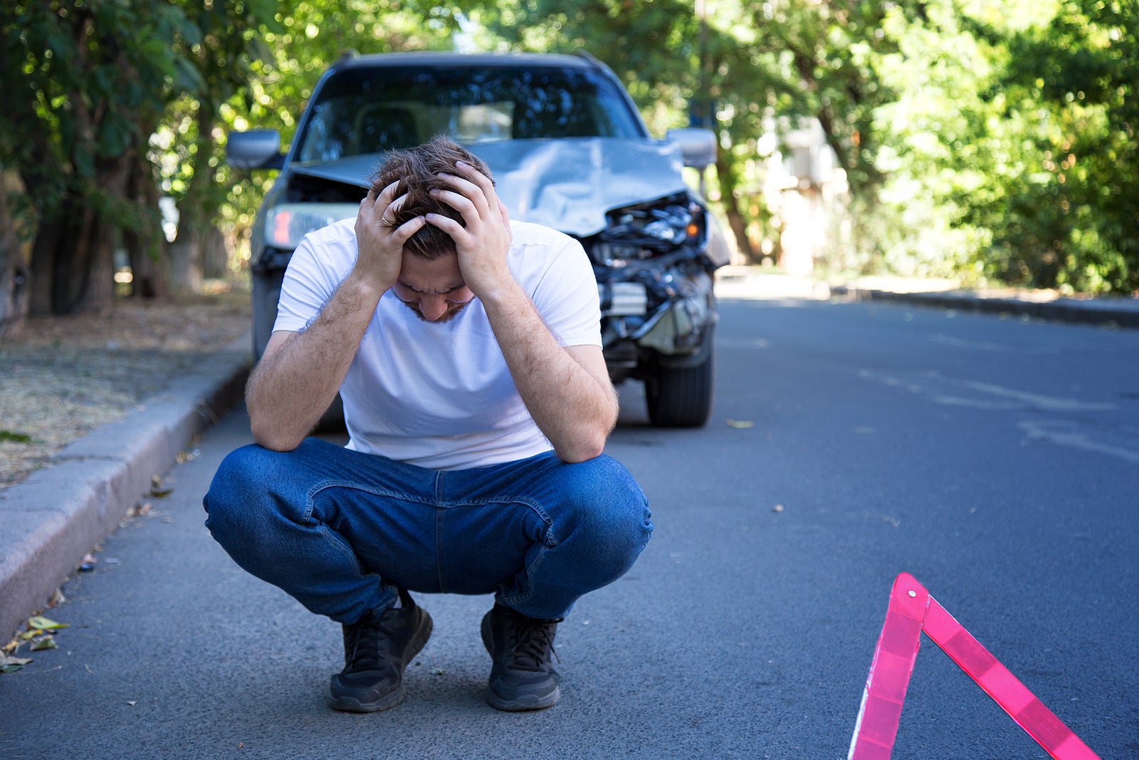 Driver man in front of wrecked car in car accident. Scared man holding his head after auto crash. Tragedy car collision. Dangerous road traffic situation.