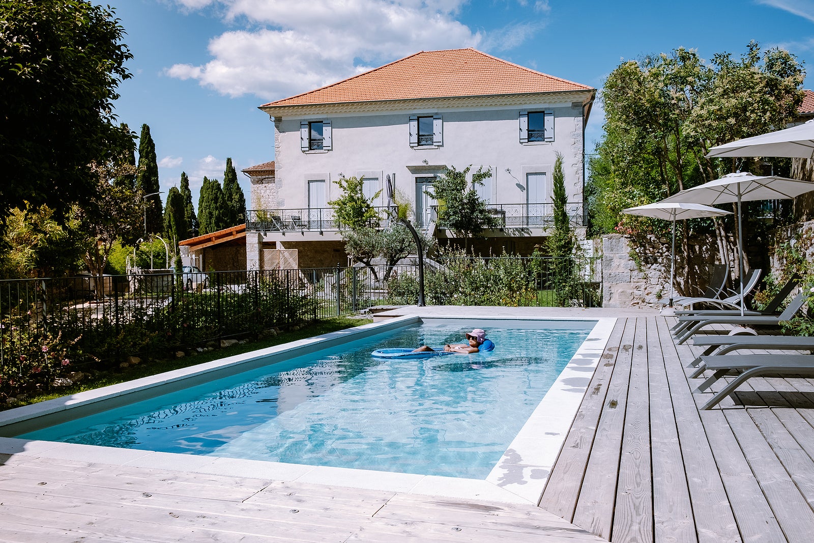 French vacation home with wooden deck and swimming pool in the Ardeche France. woman relaxing by the pool with wooden deck during luxury vacation at an holiday home in South of France