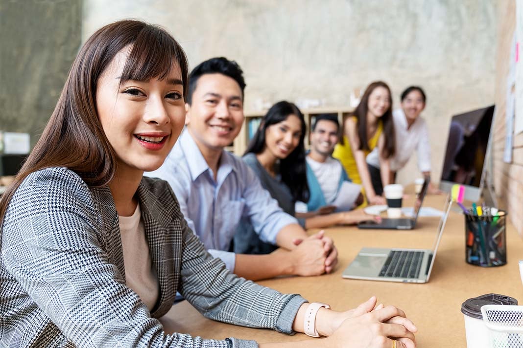 Happy asian woman and creative team are smiling and looking at camera in modern workspace office. Happy group of confident employee in cowork. Relation and engagement concept.