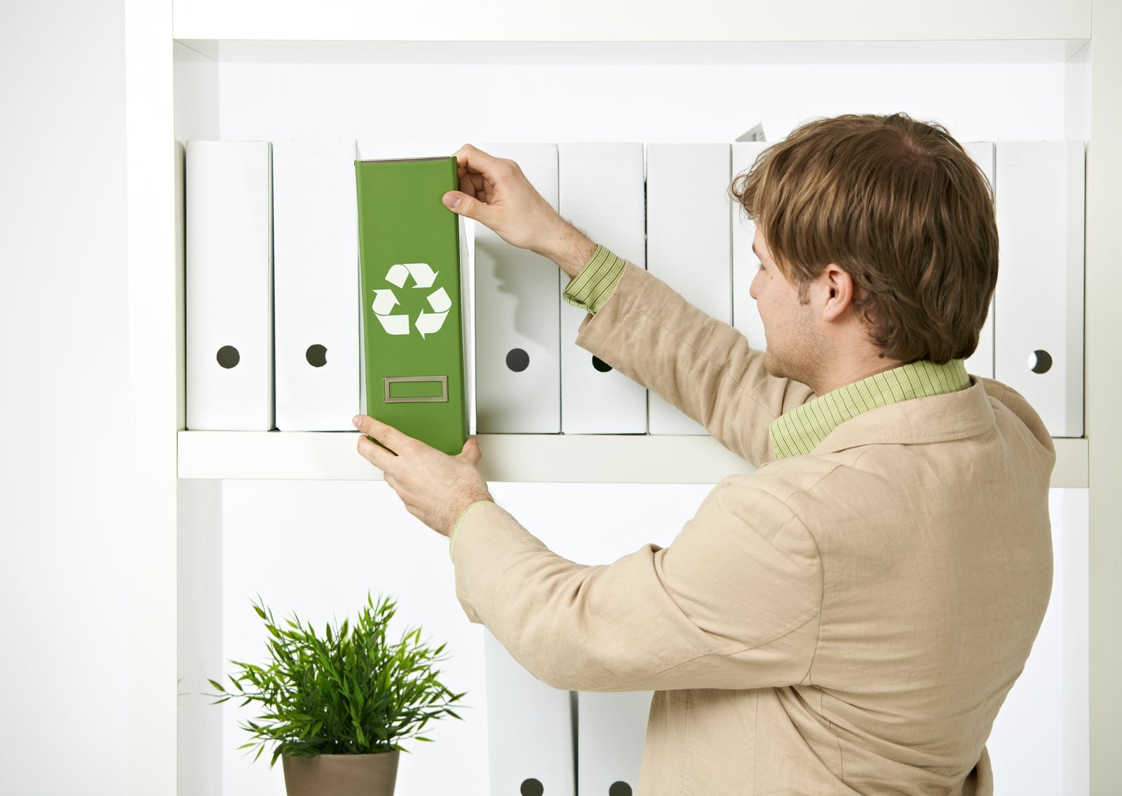 Man drawing out green folder with recycling symbol in office.?