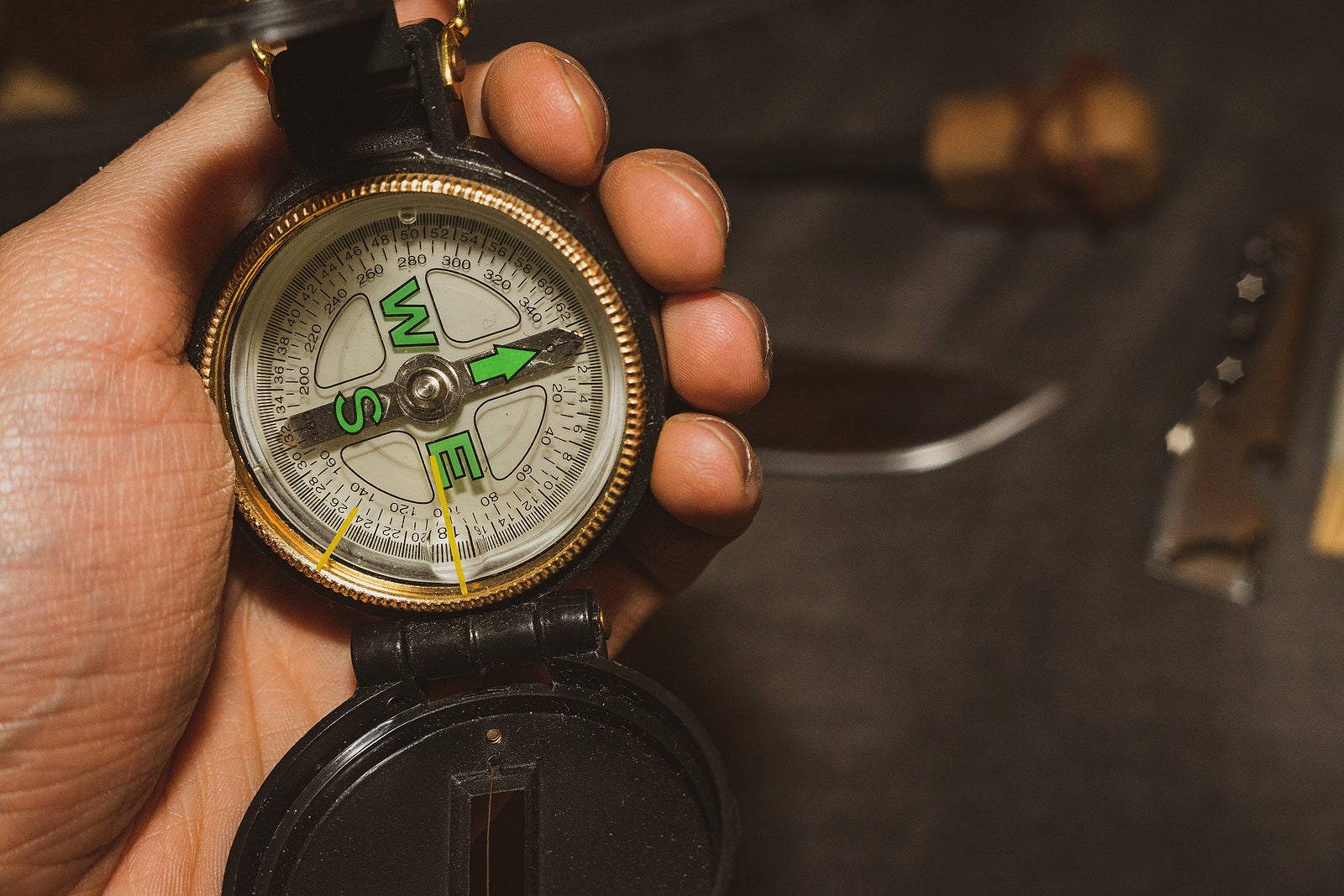 military compass in hand. Bushcrafters holding the compass in hand on background of the knife and flint. survival in extreme conditions. knife and hunting matches visible in the background