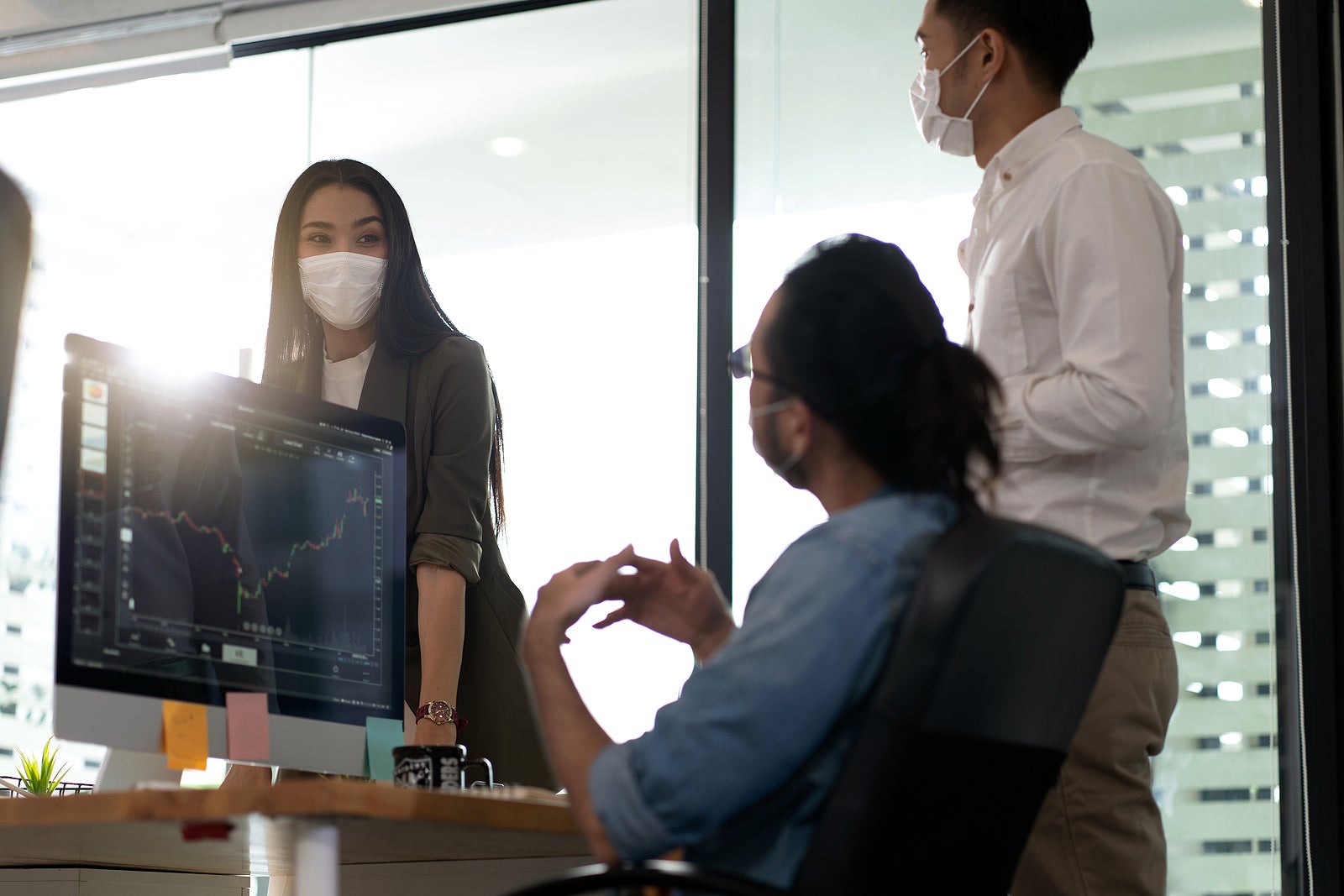 Three asian business person discuss their work in morning after office reopen due to coronavirus COVID-19 pandemic. They wear protective face mask to prevent infection. New normal office life concept.