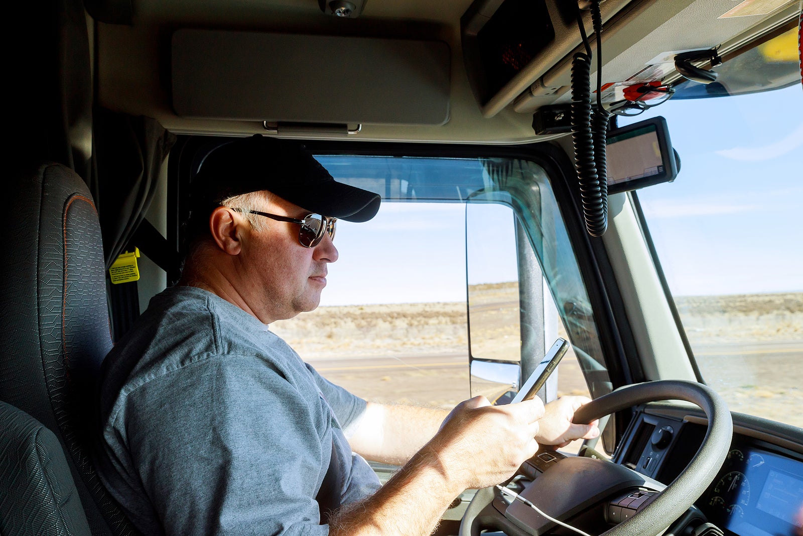 Truck drivers big truck driver holds the phone in cabin of modern truck vehicle on highway