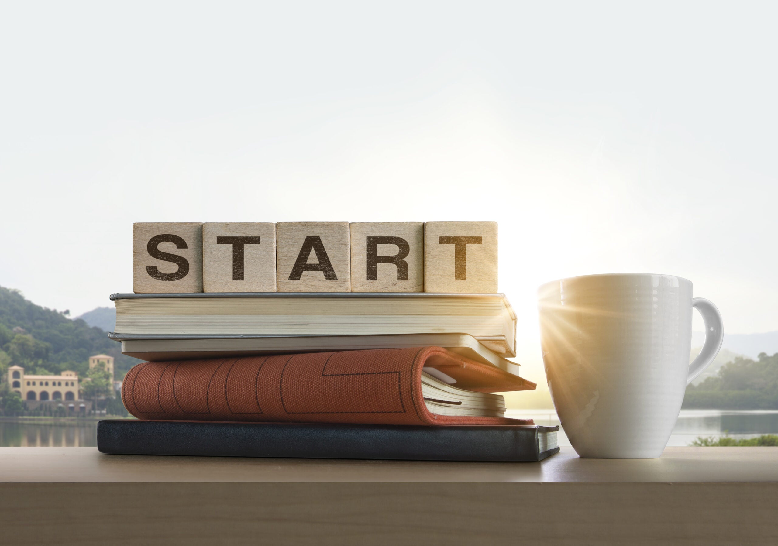 Wooden blocks with the word START, notebook, books and coffee on table with panoramic landscape background in the morning. Start, Start up, business, mindset concept.