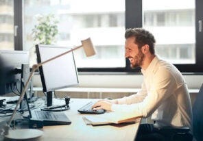 A man sitting at a desk smiling while working on the computer.